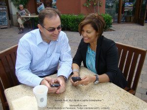 A man and woman sitting at a table looking at their cell phones.