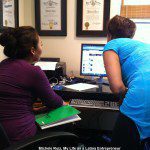 Two women sitting at a desk in front of a computer.